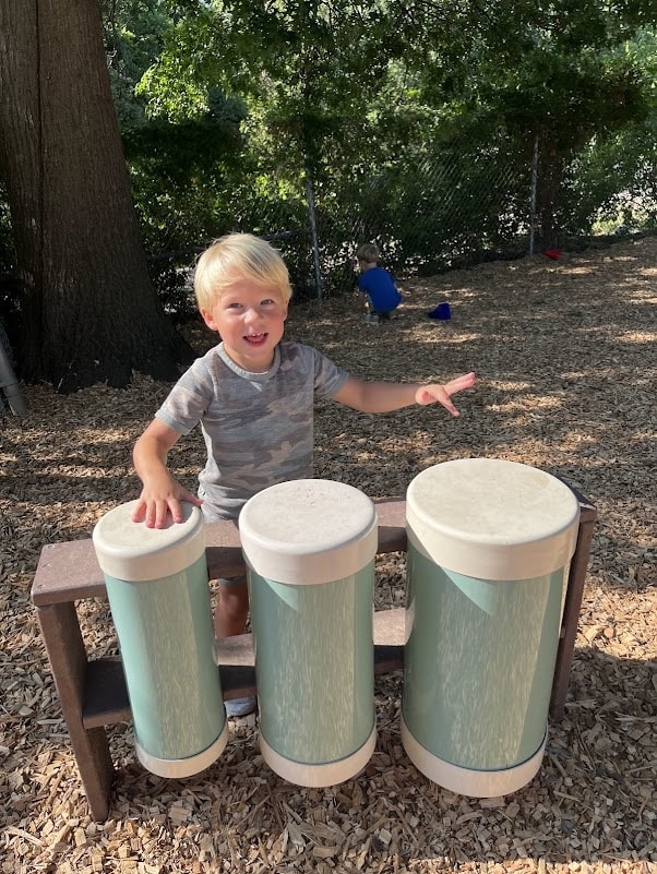 preschool boy playing large variable sized cylinders outside