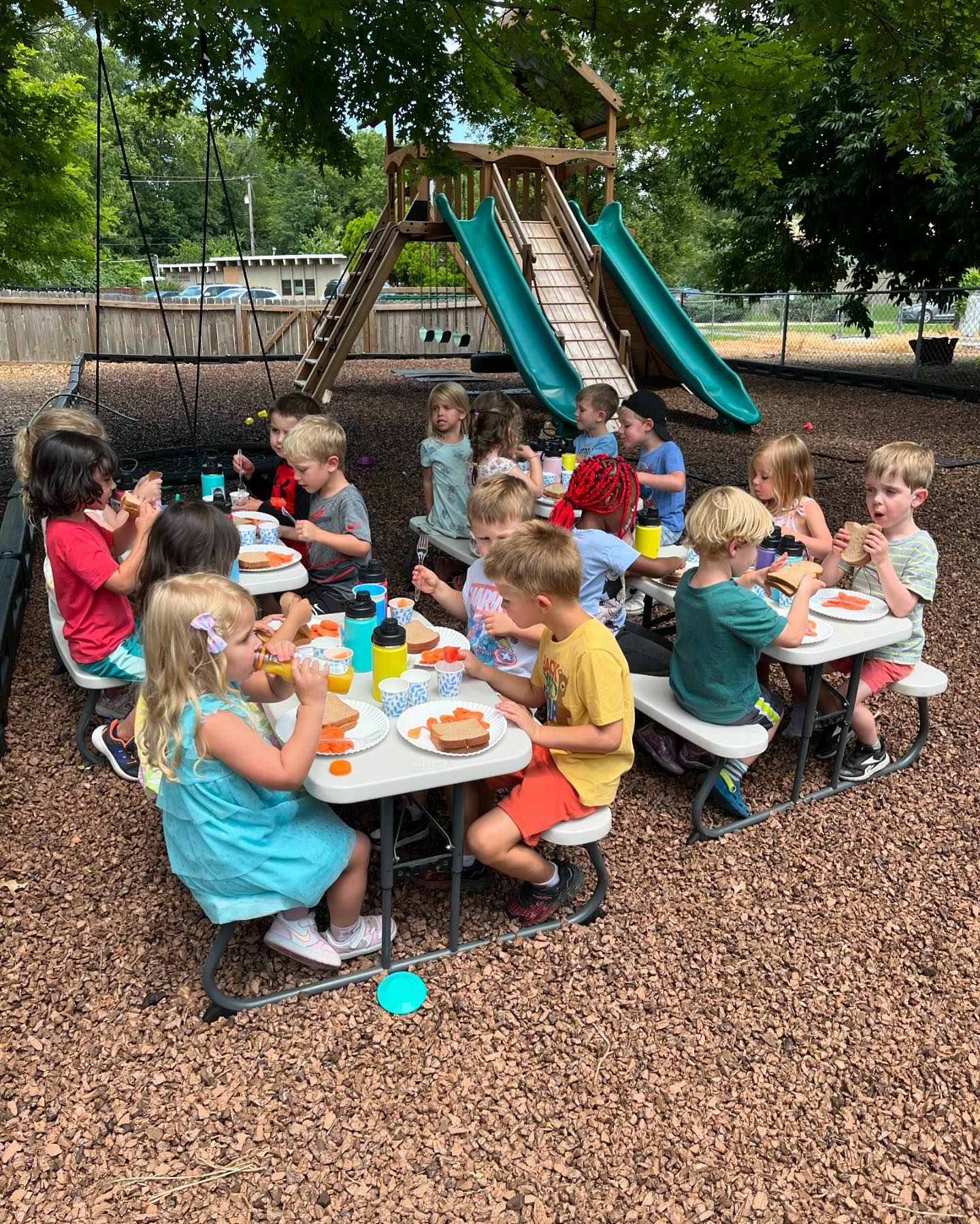 Classroom community eating lunch together outside on the picnic tables on a beautiful day.