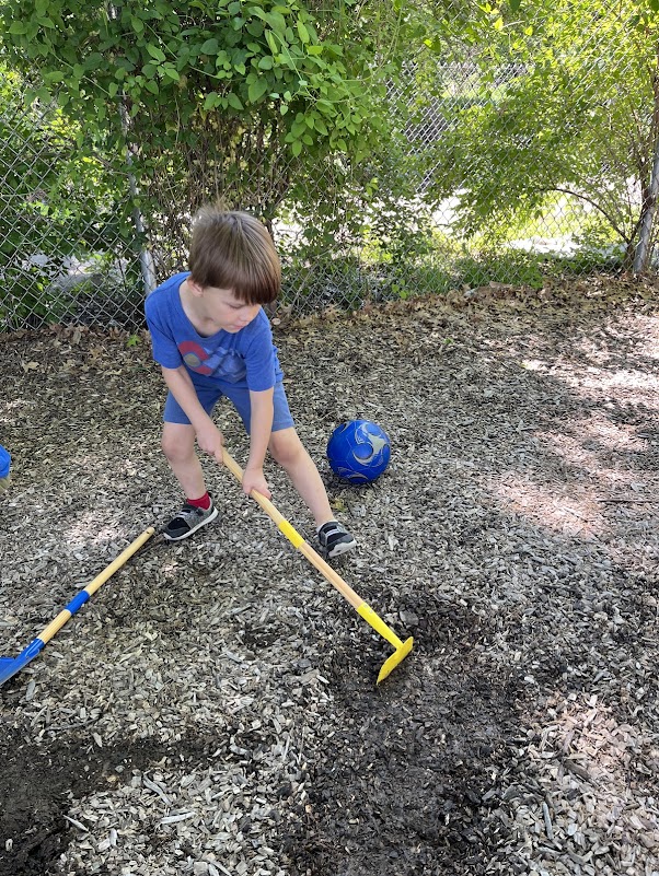 Practical Life activity, boy using hoe in outdoor play space