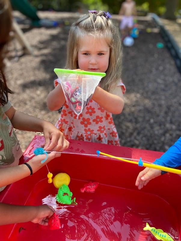 Preschool student doing water play fishing and using a net to catch fish.