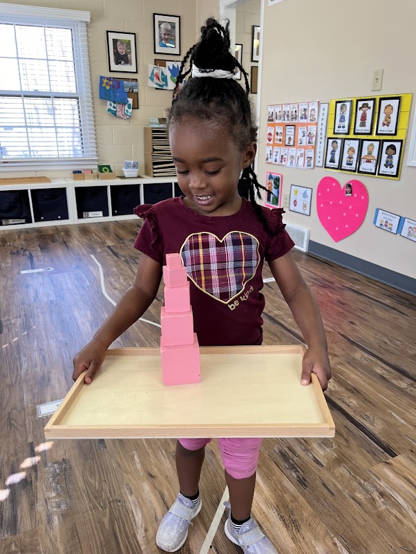 student walking a wiggly line holding a tray with stacked building blocks